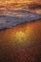 Gold and rainbow water on the sand at the beach. Retreating ocean wave casting shadow at sunset.