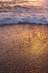 Gold and rainbow water on the sand at the beach. Retreating ocean wave casting shadow at sunset.