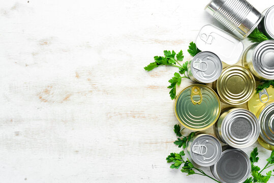 Canned food in tin jars on white wooden background. Top view.