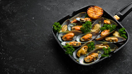 Frying pan with fried mussels with garlic, parsley, lemon and spices. On a black stone background. Free space for text.