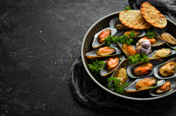 Boiled mussels in garlic sauce with parsley and lemon. Seafood. On a black stone background.