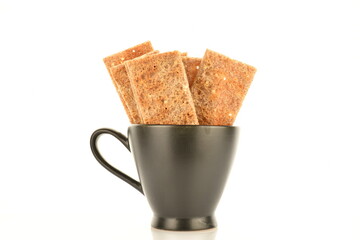 Fototapeta na wymiar Several multigrain thin crisps in a black cup, close-up, isolated on white.