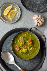 Traditional Indian Punjabi food Palak Paneer with spinach and cheese in vintage metal bowl with spoon on rustic grey concrete background table from above 
