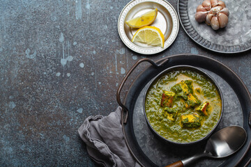 Traditional Indian Punjabi food Palak Paneer with spinach and cheese in vintage metal bowl with spoon on rustic concrete background from above with space for text