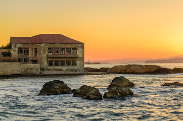 Beautiful Sunset in Chania, Greek Island of Crete, Greece.  Small Bay with an Abandoned Building. Sun is Behind the Mountains. Nice Colors in the Sky and Sea.