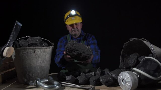 A miner turns a large lump of black coal in his hands