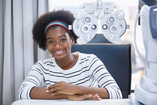 Happy young woman african american eye exam with diagnostic ophthalmology in optical clinic. professional ophthalmic checking vision. phoropter machine, Eye health check and ophthalmology concept.