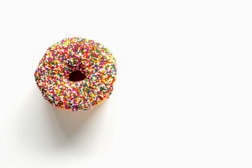 Donut with colorful sprinkles on white background with copy space.