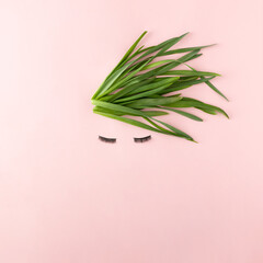 Face made with eyelashes and hair of green leaves on pastel pink background. Minimal nature concept. Creative idea.