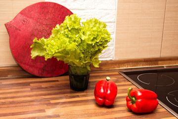 Two red bell peppers and green lettuce leaves on the kitchen table, healthy food.