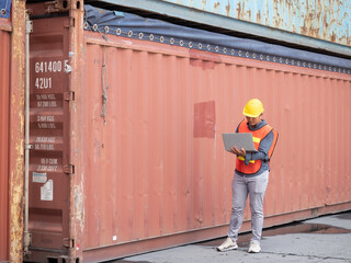 Inspection Asian engineer is using a laptop computer and wearing a yellow safety helmet and check for control loading containers box from Cargo freight ship for import and export..