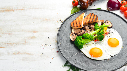 Healthy breakfast. Fried egg with broccoli, mushrooms and bread. On a black stone plate. Top view.