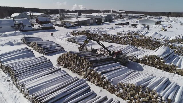 aerial photography of unloading logs from a car trailer using a manipulator and storing logs in an open area in winter