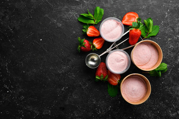 Strawberry ice cream with mint and strawberries. Ice cream spoon. On a black stone background, top view.