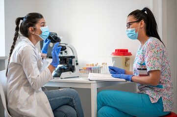 Two lab women technicians working together in the laboratory and using a microscope. 
