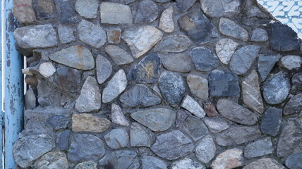 a fragment of a stone fence made of natural large cobblestones of different shades, a detail of the exterior space made of rough rough stones in the structure of an old hedge facade