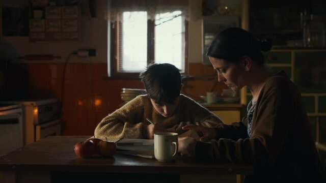 Portrait of sad poor mature mother helping small daughter with school indoors at home, poverty concept.