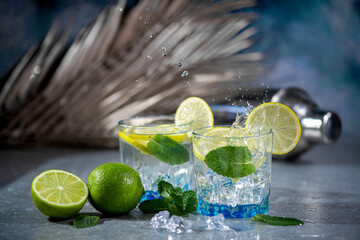 Summer alcoholic cocktail mojito or gin tonic with rum, mint, lime and ice, bar tools on concrete...