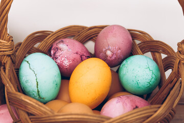 Easter eggs in a basket. An Easter basket with yellow, green and purple eggs and decorated with snowdrops stands on a wooden table. Easter background.