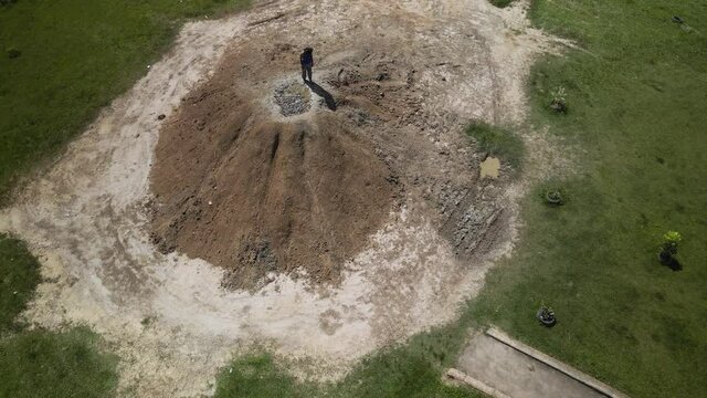 Epic aerial of an East Indian woman standing on a cone shaped mud volcano located in Penal, Trinidad