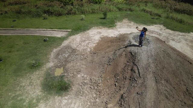 Aerial view of a young girl standing and taking selfies on a mud volcano located in Penal, Trinidad