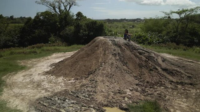 Aerial 360 pan of a girl sitting on a cone shaped mud volcano on the tropical island of Trinidad