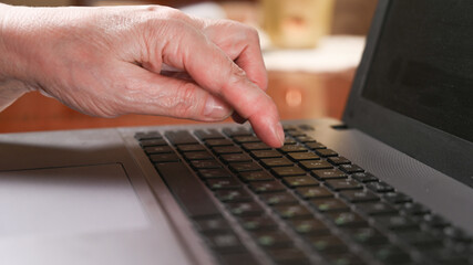 Elderly woman is typing on a laptop. Close-up of hand and keyboard