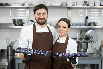 Couple of loving confectioners, a man and a woman, embrace and hold a chocolate cake decor in their hands.