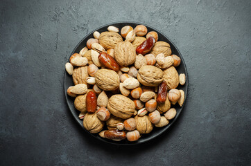 Nuts and dates in a plate on a dark concrete background. Source of vegetable protein and vitamins.