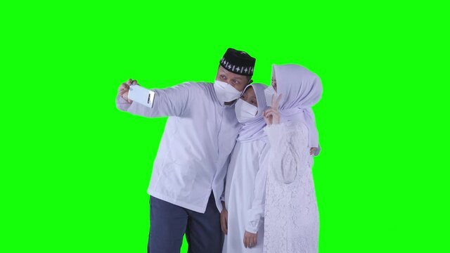 Muslim child and parents in face mask taking selfie
