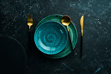 Turquoise plate and cutlery on a black stone background. Top view. Rustic style.