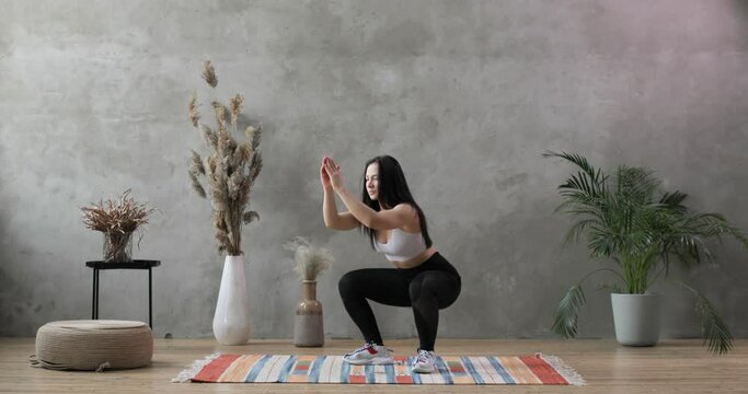 Young woman goes in for sport on the background of a gray concrete wall. She does squats. Healthy lifestyle and sport concept.