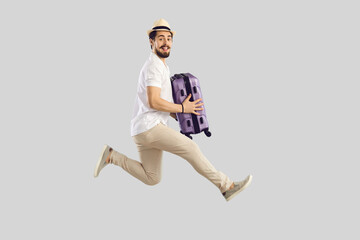 Passenger traveling on weekend, air flight journey concept. Funny cheerful excited man traveler tourist in summer hat jumping hold suitcase luggage. Full length studio portrait on grey copy space