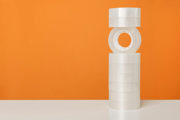 Adhesive sticky tape on white table against bright orange background. Minimalistic, vivid colors. Office supplies.