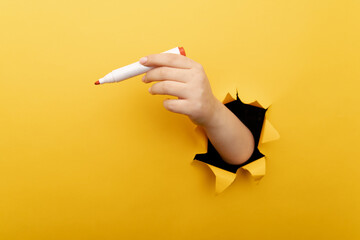 A hand with marker though a broken yellow paper wall.