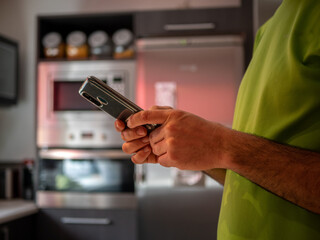 Spanish man sending a message with his phone in the kitchen