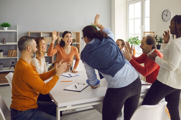 Team of diverse people, colleagues and business partners, celebrating success in office meeting. Group of excited young and mature workers high fiving each other happy hard work and teamwork paid off