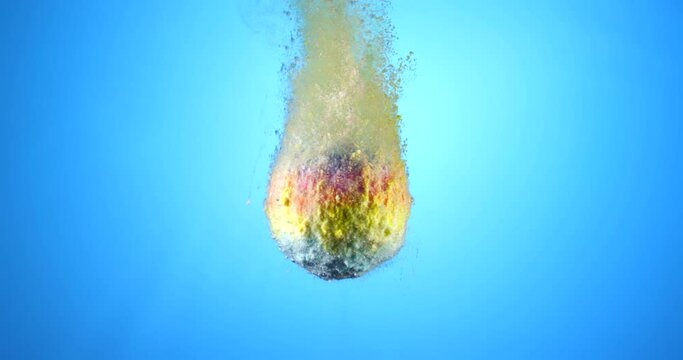 Colorful bath bomb falling down into clean water against blue background. Filmed in slow motion with RED camera