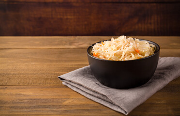 Black bowl with sour sauerkraut on gray napkin on wooden brown background close up with copy space