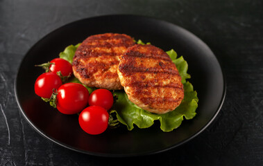 Fried cutlet with lettuce and tomatoes in a black plate on a black background