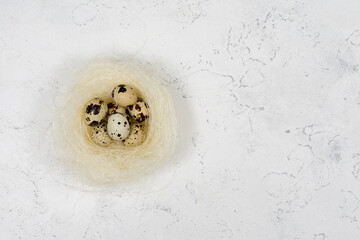 Three quail eggs in a nest on a white concrete background. Place for an inscription.