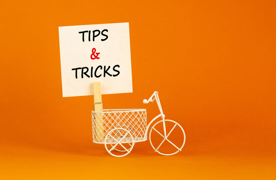 Tips and tricks symbol. White paper. Words 'Tips and tricks'. Miniature bicycle. Beautiful orange background. Business and tips and tricks concept, copy space.