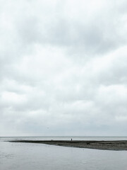 Alone man walking on pebble beach at windy weather. Grey cloudy sky upon seaside.