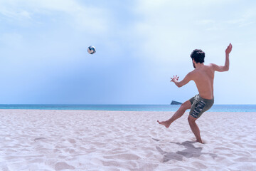 Young man on the beach shoots the ball into the sea on his summer vacation.
