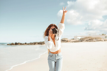 Beautiful woman taking pictures with a professional camera while walking at the beach - 426158469