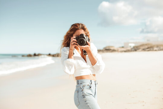 Beautiful woman taking pictures with a professional camera while walking at the beach