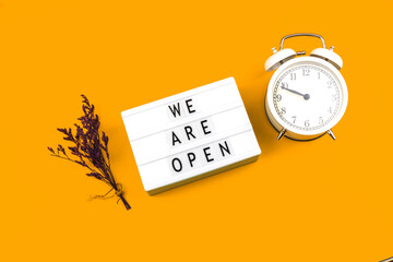 Creative flat lay sign We are open with alarm clock and flowers, top view, business and cafe notification concept