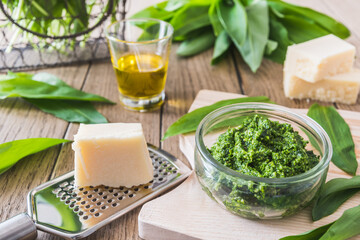 Homemade wild garlic pesto in a glass bowl on wooden background, decorated with leaves, parmesan cheese and olive oil
