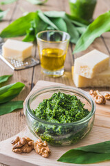 Homemade wild garlic pesto in a glass bowl on wooden background, decorated with leaves, parmesan cheese and olive oil, vertical