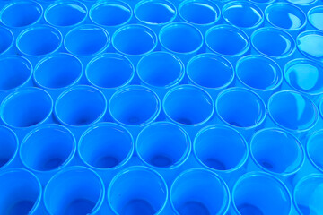 Clear water in blue plastic disposable cups. Abstract background.